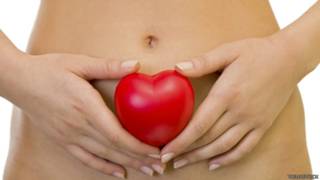 Una mujer que sostiene una forma de corazón sobre su vientre