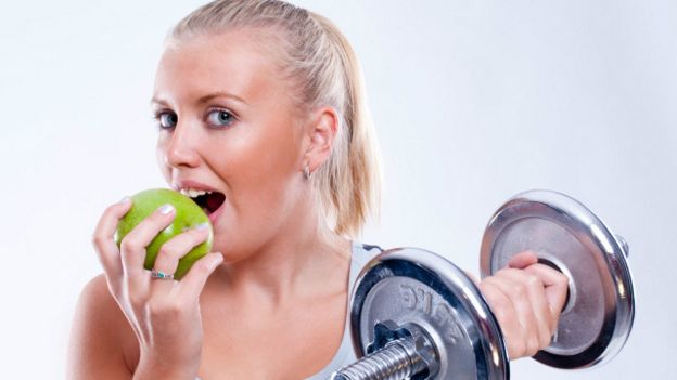 Una joven comiendo una manzana y levantando una pesa