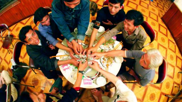 Hombres vietnamitas toman chupitos de vino de serpiente en un hostal.