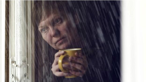Una persona mira llove con una taza en la mano